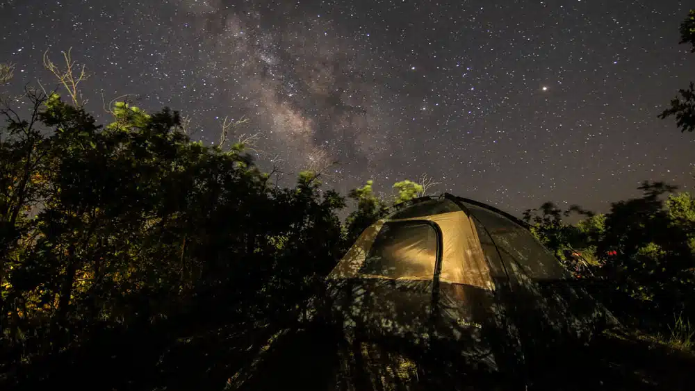A tent is illuminated under a starry sky featuring the Milky Way.